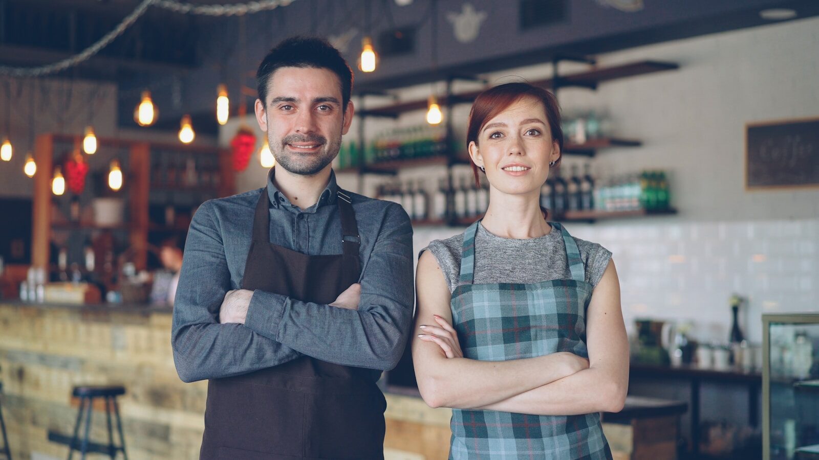 Two people pose confidently in a coffee shop.